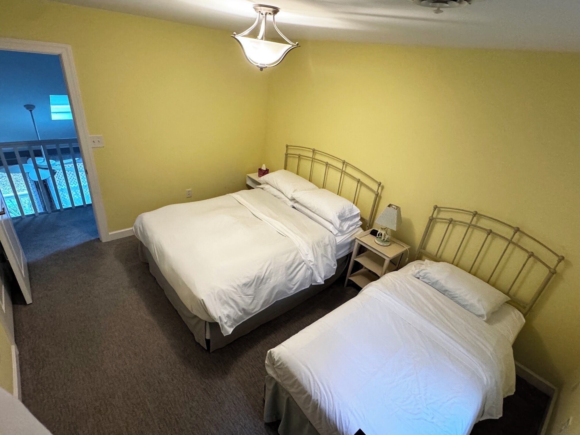 A hotel room with two beds, a nightstand, a lamp, and a ceiling light.