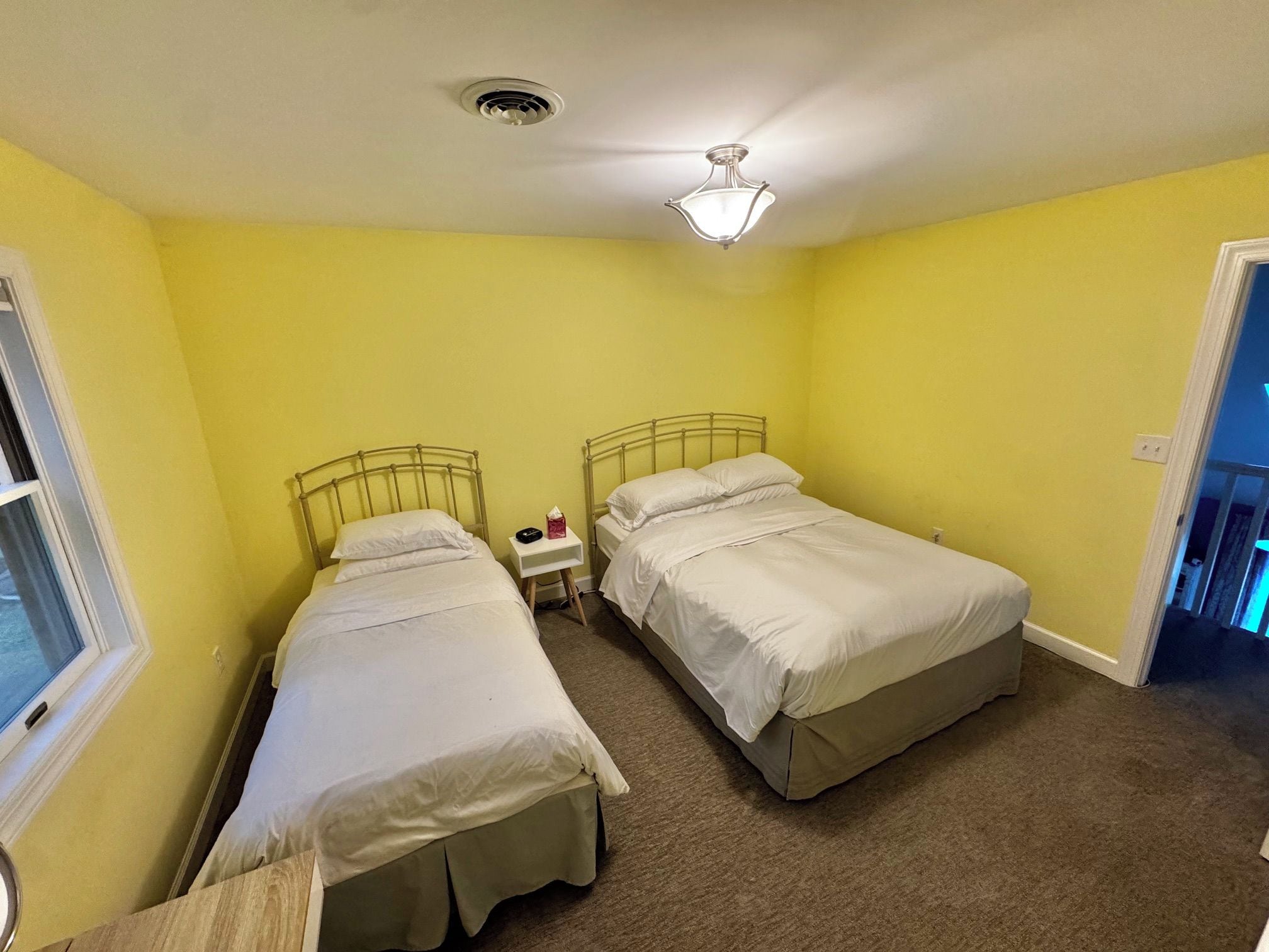 A small, single-room accommodation with two beds, a ceiling fan, and a window.