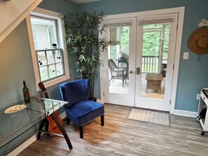 A room with a glass table, a blue chair, a guitar, a plant, and a door leading to an outdoor area. - Stylish home w all the comforts in a bay front community near beaches & shopping (Lewes)