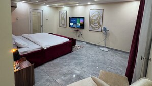 A hotel room with a bed, a TV mounted on the wall, a standing fan, and a seating area with a chair. - 4 Bed Luxury Town House (Lagos)