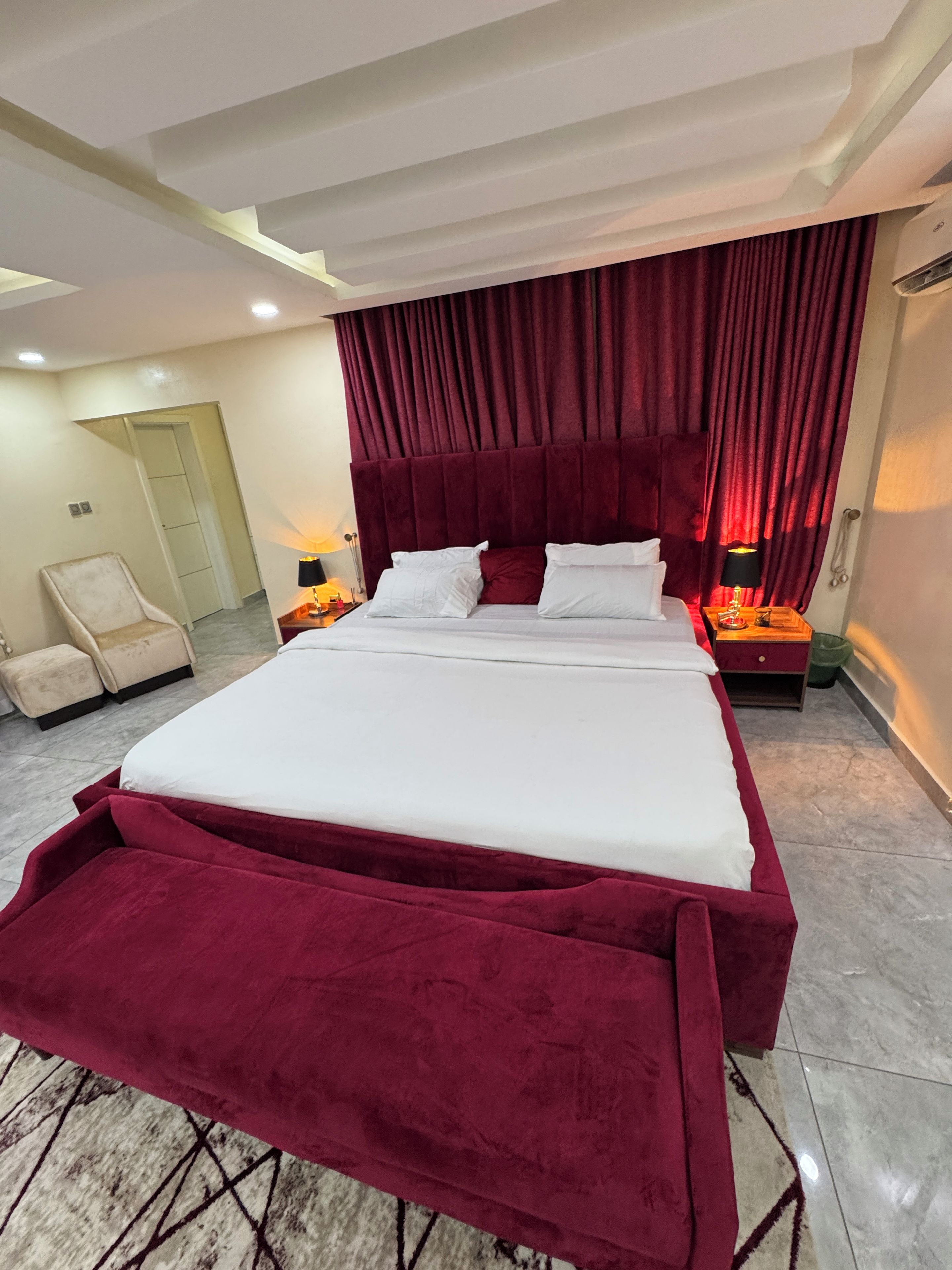Een hotelkamer met een groot bed, een stoel, een nachtkastje met een lamp en een gordijn.