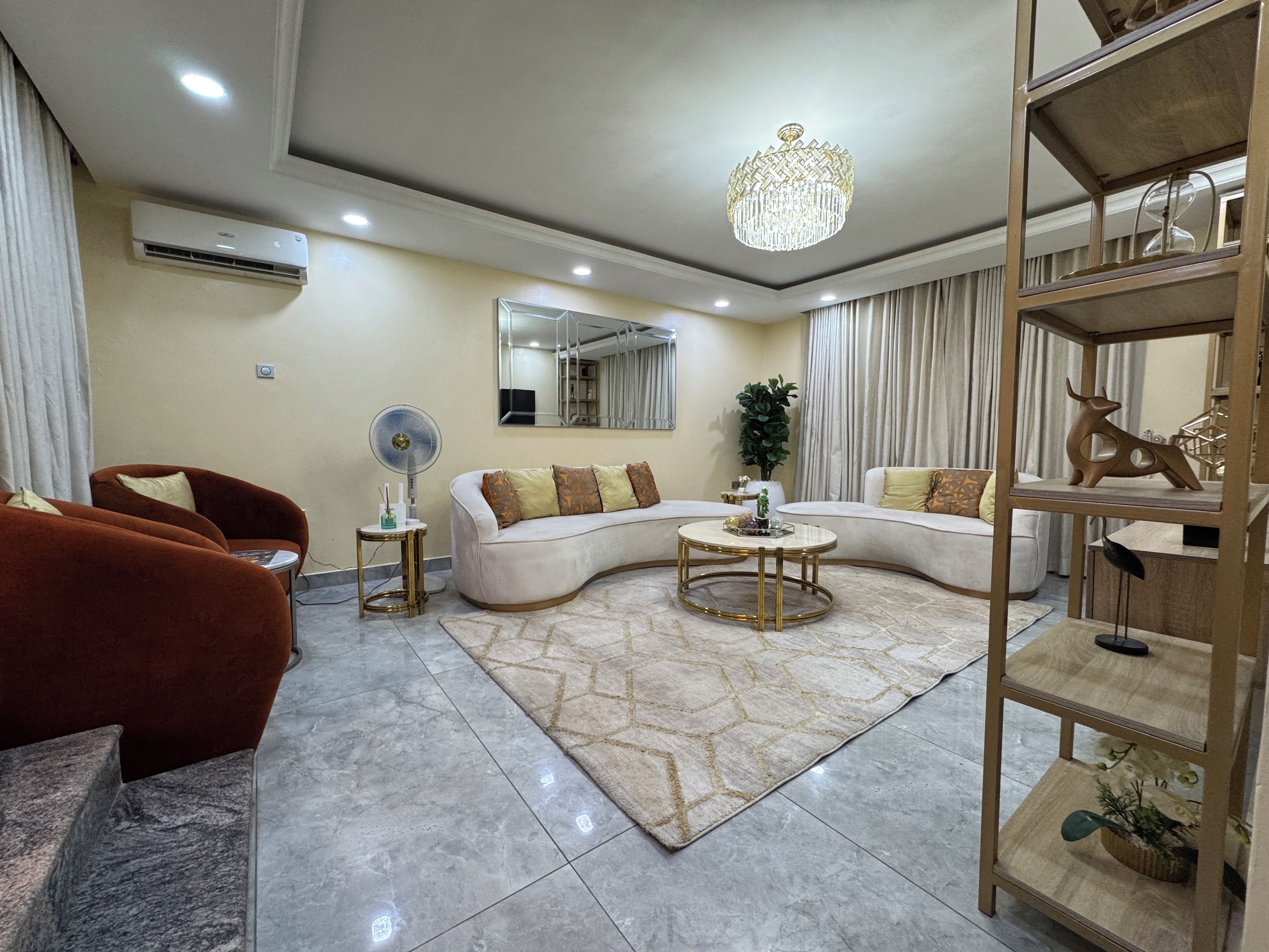 Un salon moderne avec un canapé d’angle, une table basse ronde, un lampadaire et une étagère décorative.
