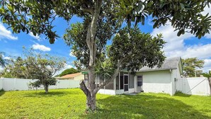 A residential property with a well-maintained lawn, a single-story house with a front door, and a white fence surrounding the property. - Cozy home New Port Richey (New Port Richey)