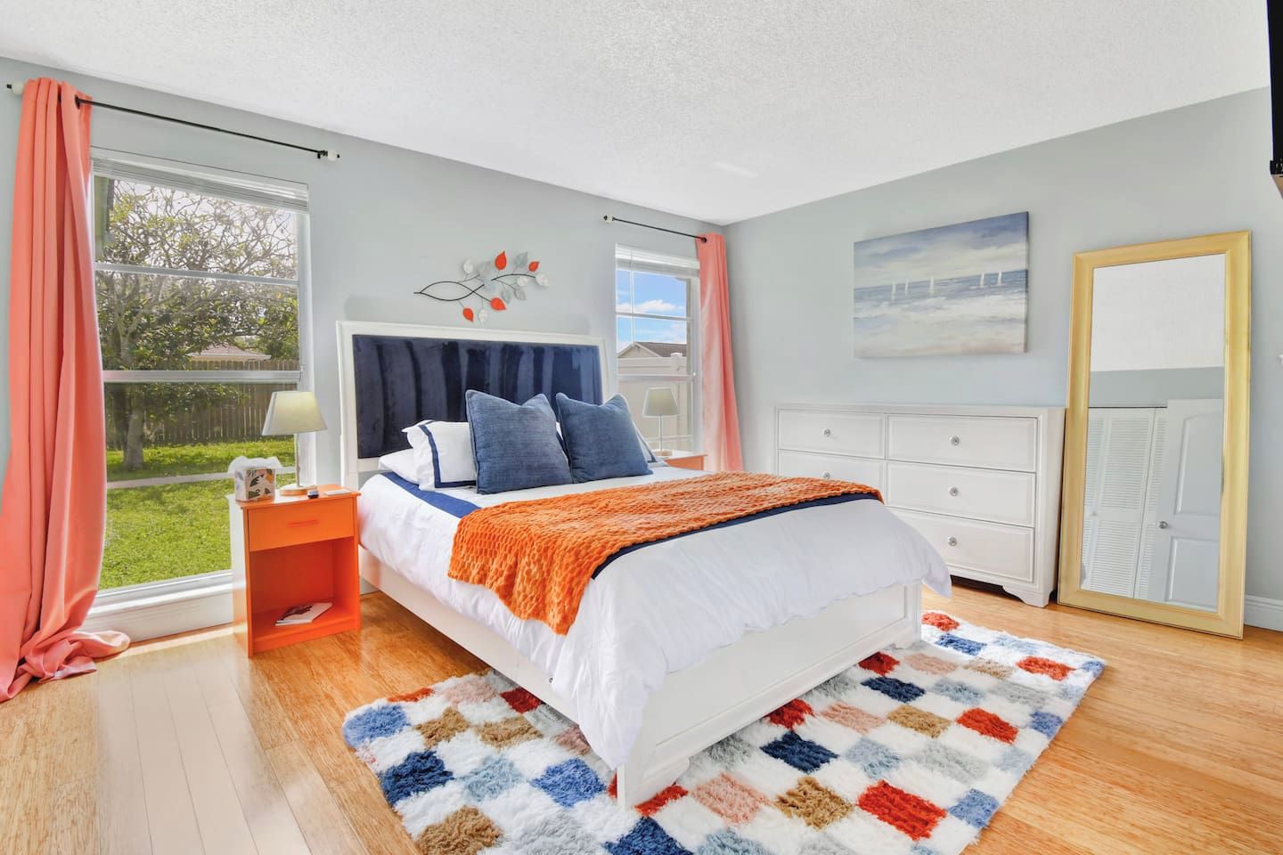 A bedroom with a bed, a nightstand, a dresser, a window with curtains, and a painting on the wall.