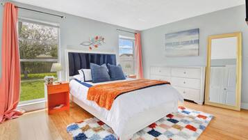 A bedroom with a bed, a nightstand, a dresser, a window with curtains, and a painting on the wall.