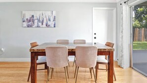 A dining area with a wooden table and four chairs, a cityscape painting on the wall, and a sliding glass door leading to a garden. - Cozy home New Port Richey (New Port Richey)