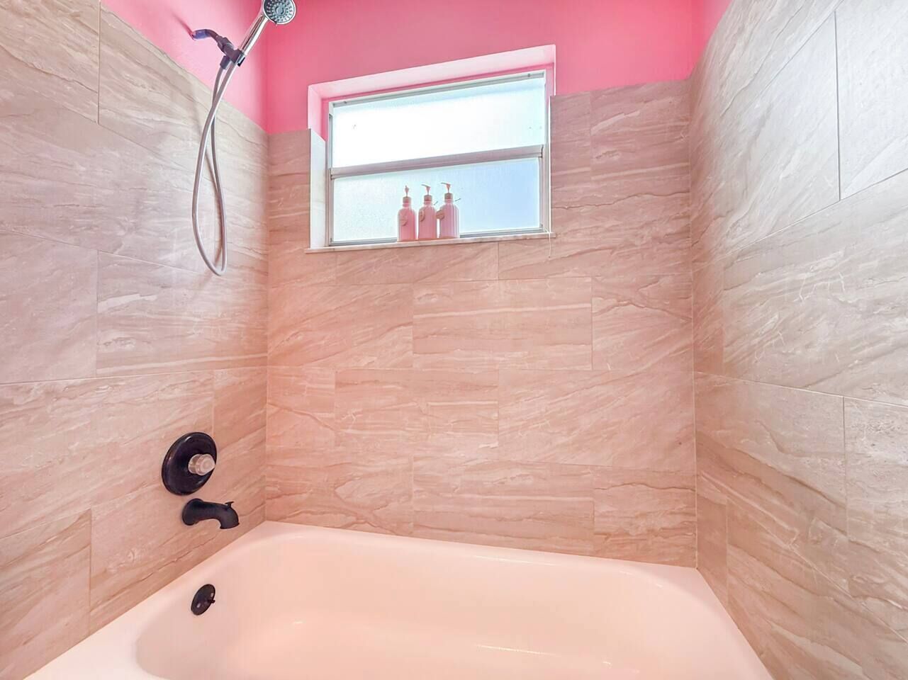 A bathroom with a bathtub, a showerhead, and a window with bottles on the sill.