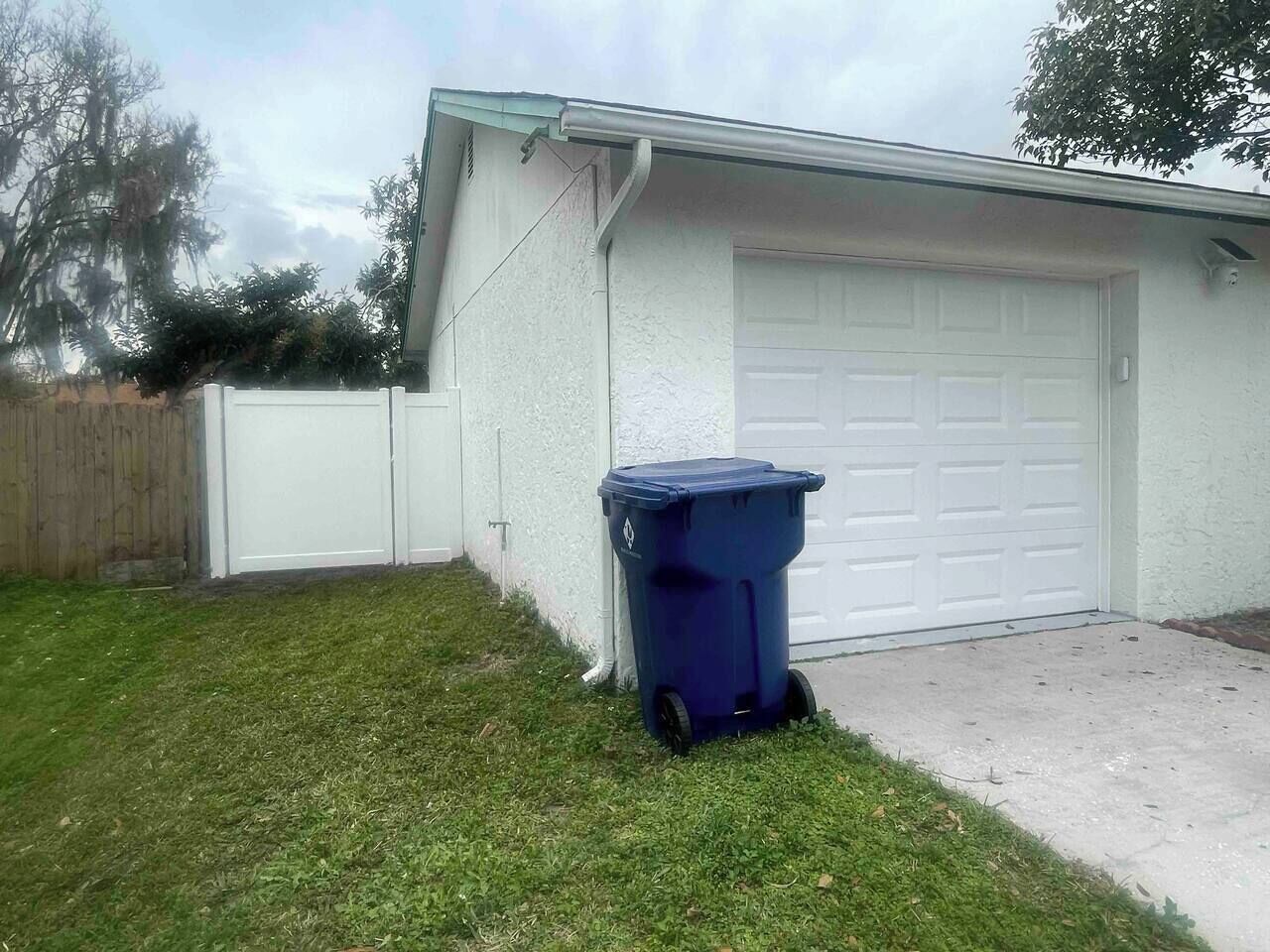 A garage with a white door, a blue trash bin, and a grassy yard.