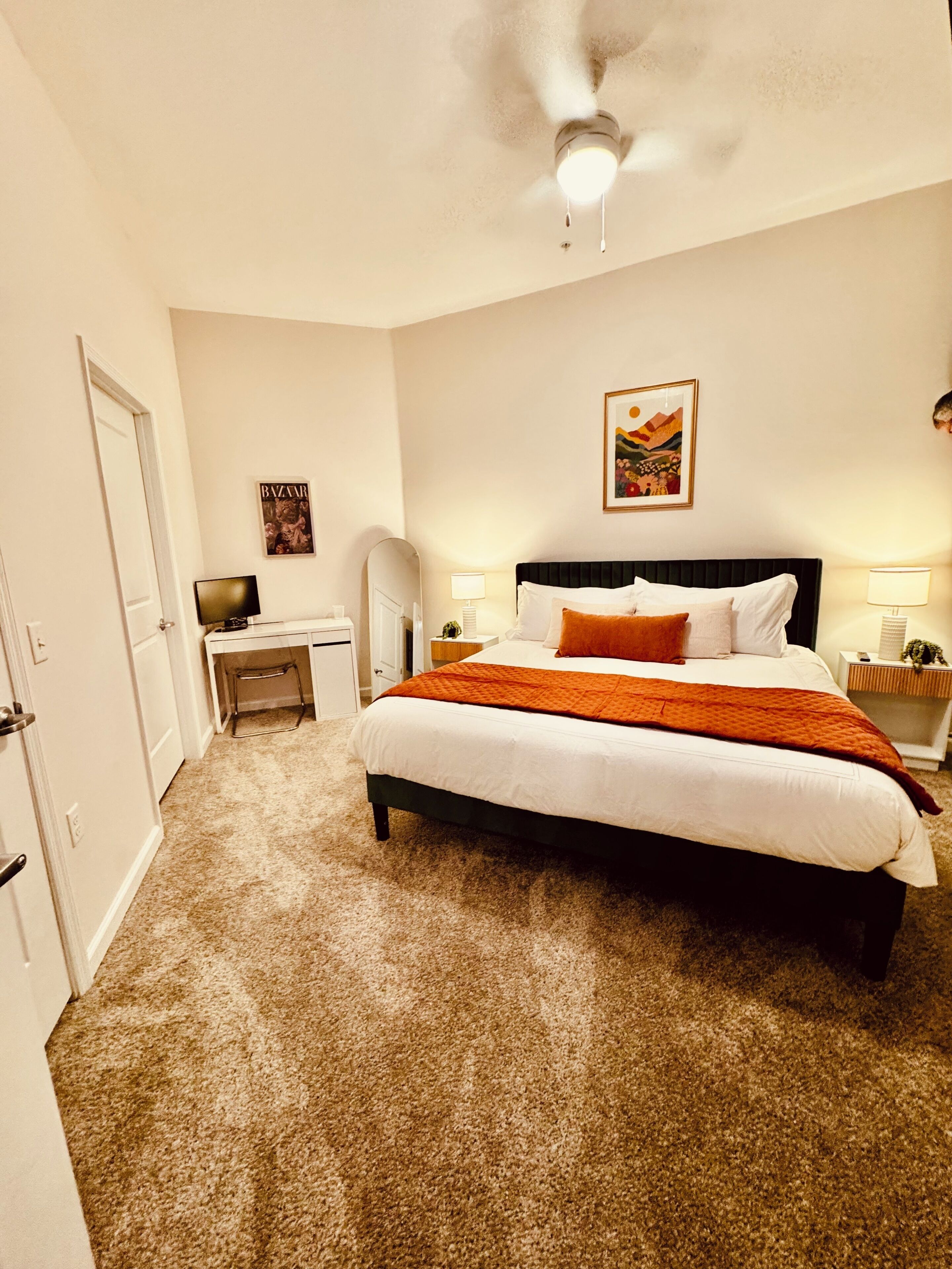 Una habitación de hotel con cama, escritorio, silla, ventilador de techo y lámpara de pared.