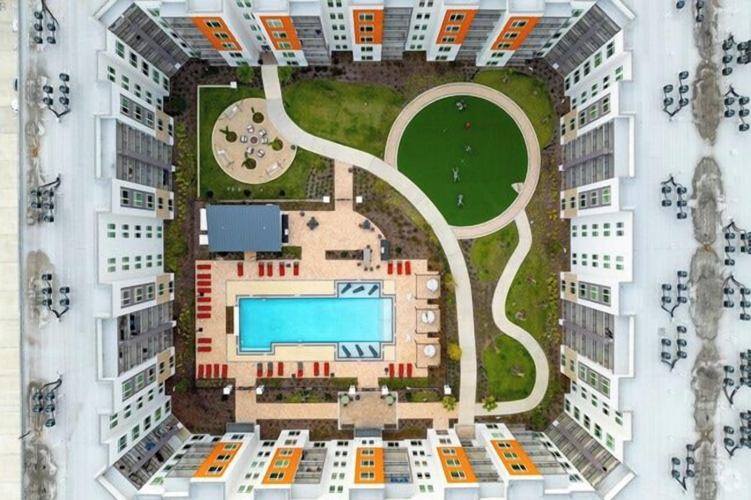 A high-rise building with a central swimming pool, multiple balconies, and a landscaped area with a circular garden.