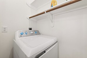 Lavadora de carga frontal blanca con perillas de control y un enchufe en la pared.