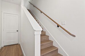 Una escalera con peldaños de madera y barandales blancos, que conduce a una puerta blanca.