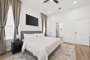 Un dormitorio moderno con una cama grande, una mesita de noche, un ventilador de techo y vistas al baño.