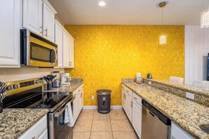 A kitchen with white cabinets, a yellow textured wall, granite countertops, and stainless steel appliances. - Paradise Oasis| Stylish 4 Bed|Pool House (Kissimmee)