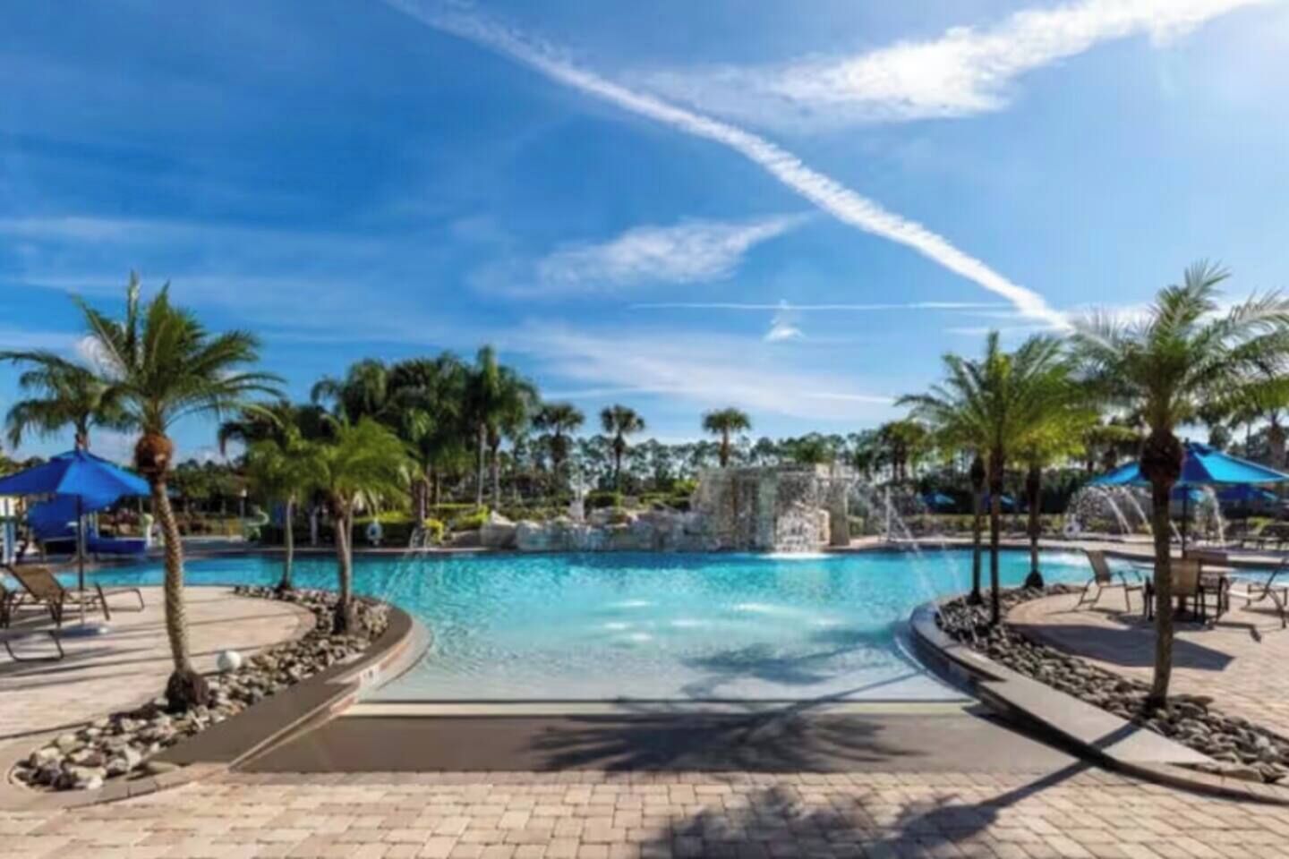 A resort pool area with palm trees, lounge chairs, and a clear blue sky.