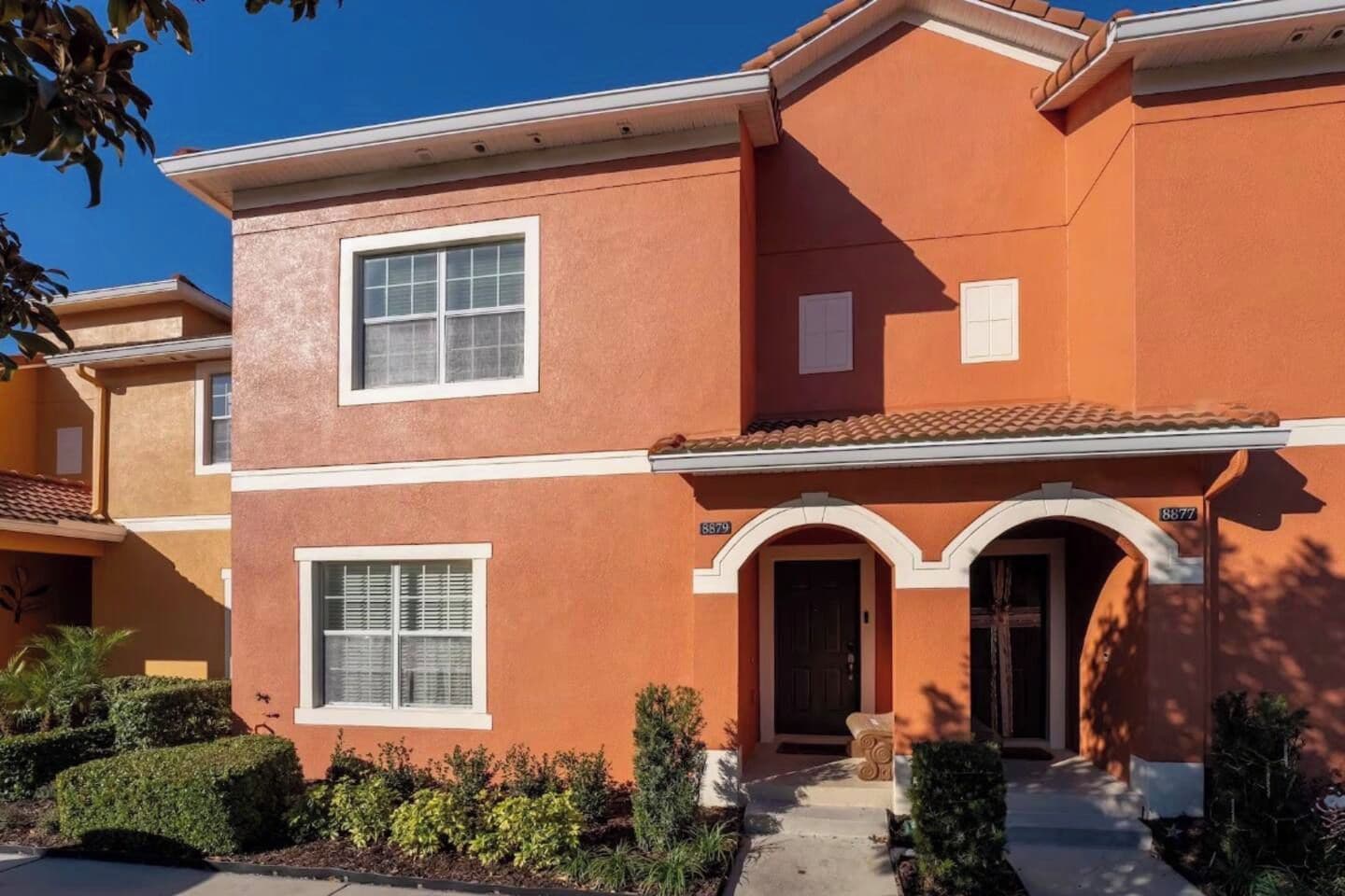 A two-story building with a red exterior, white trim, and a tiled roof. There are two visible windows with white frames, a front door with an archway, and a small porch area.