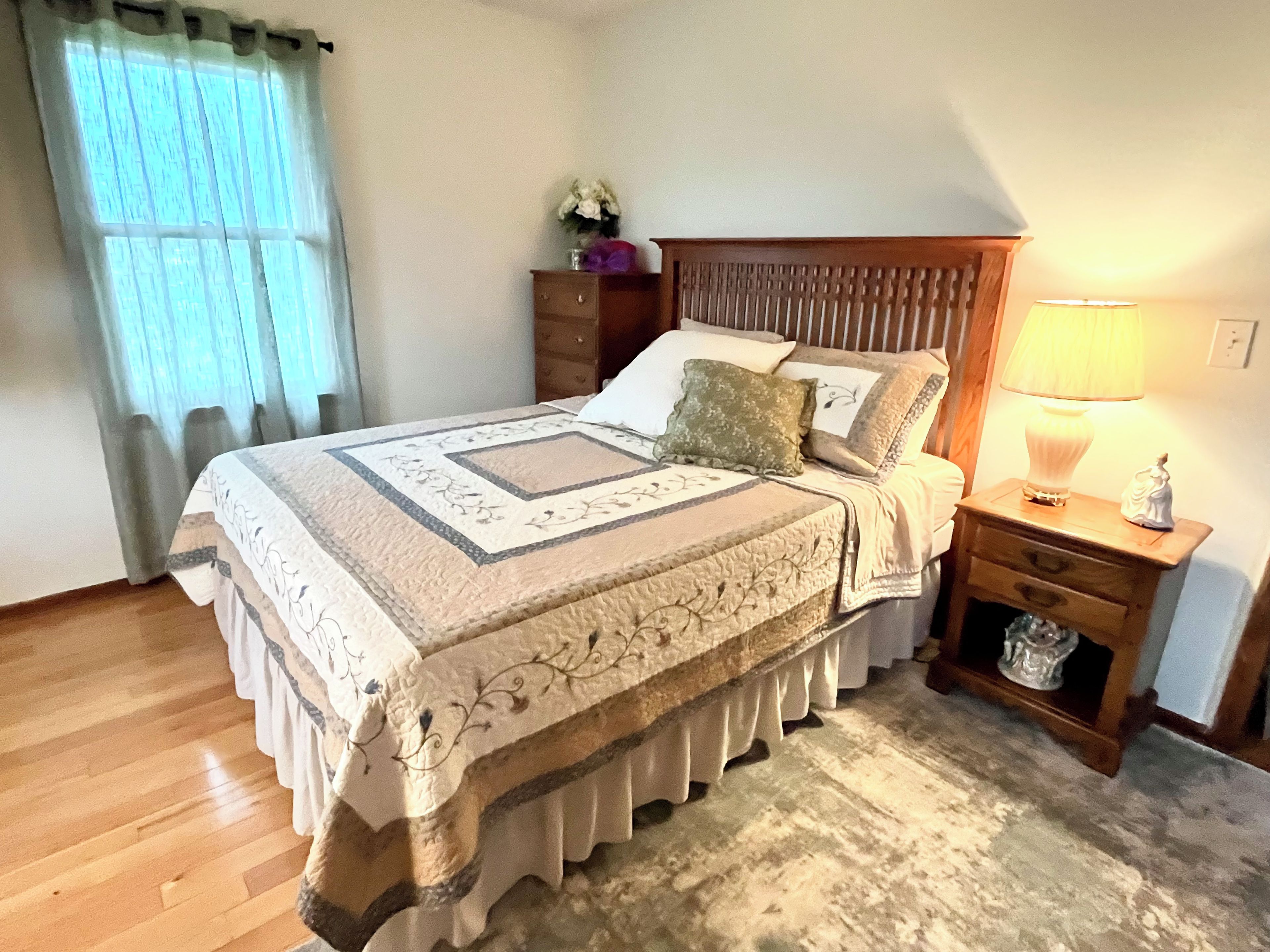 A bedroom with a bed, a nightstand, a lamp, and a dresser.