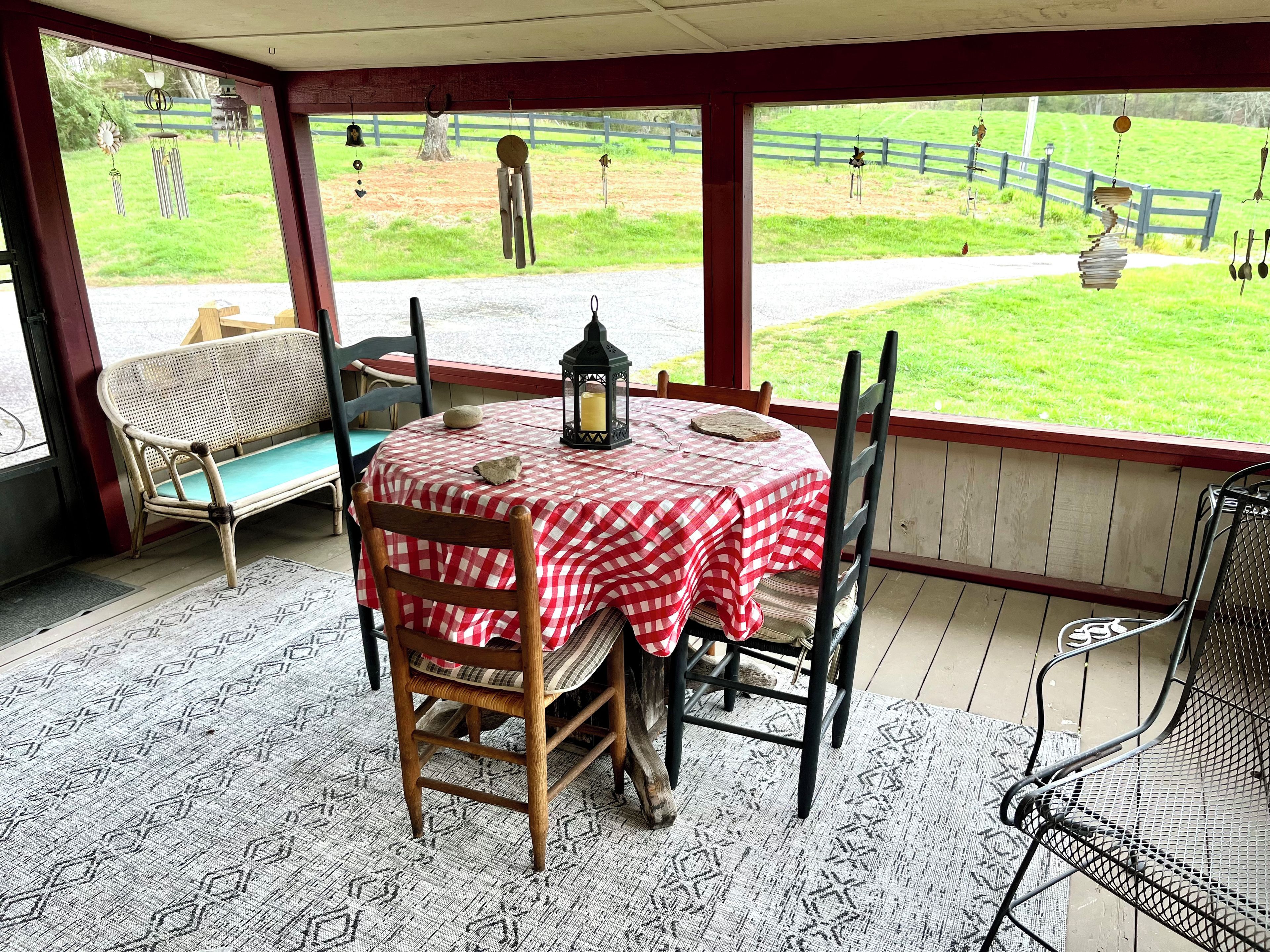 A covered patio with a table set for two, a bench, and a view of a fenced yard.