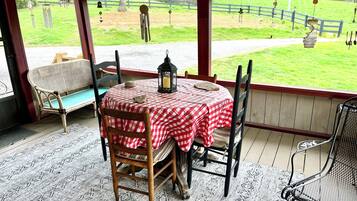 Une terrasse couverte avec une table préparée pour deux personnes, un banc et une vue sur une cour clôturée.