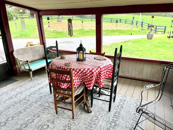 A covered patio with a table set for two, a bench, and a view of a fenced yard.