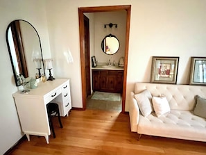 A room with a white vanity, a mirror, a white sofa, and a wooden cabinet.