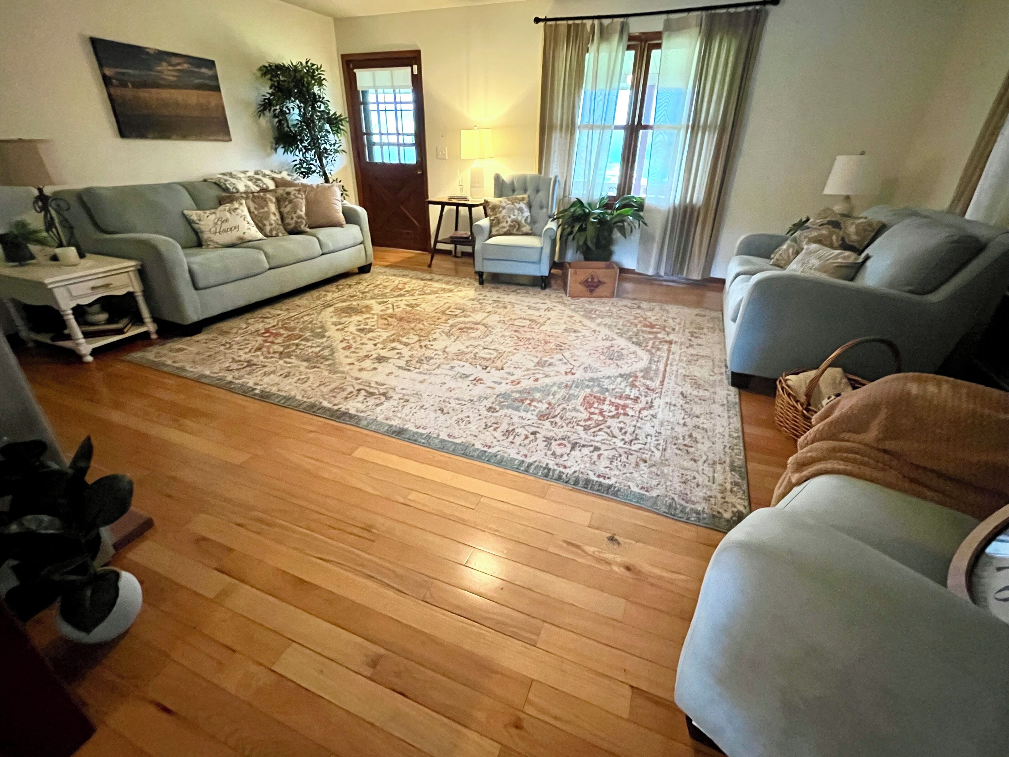 Una sala de estar con un tapete grande, dos sofás, una mesa de centro y una puerta que da a otra habitación.