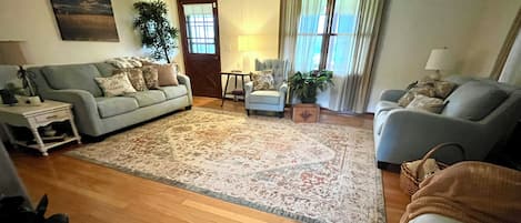 A living room with a large rug, two sofas, a coffee table, and a door leading to another room.