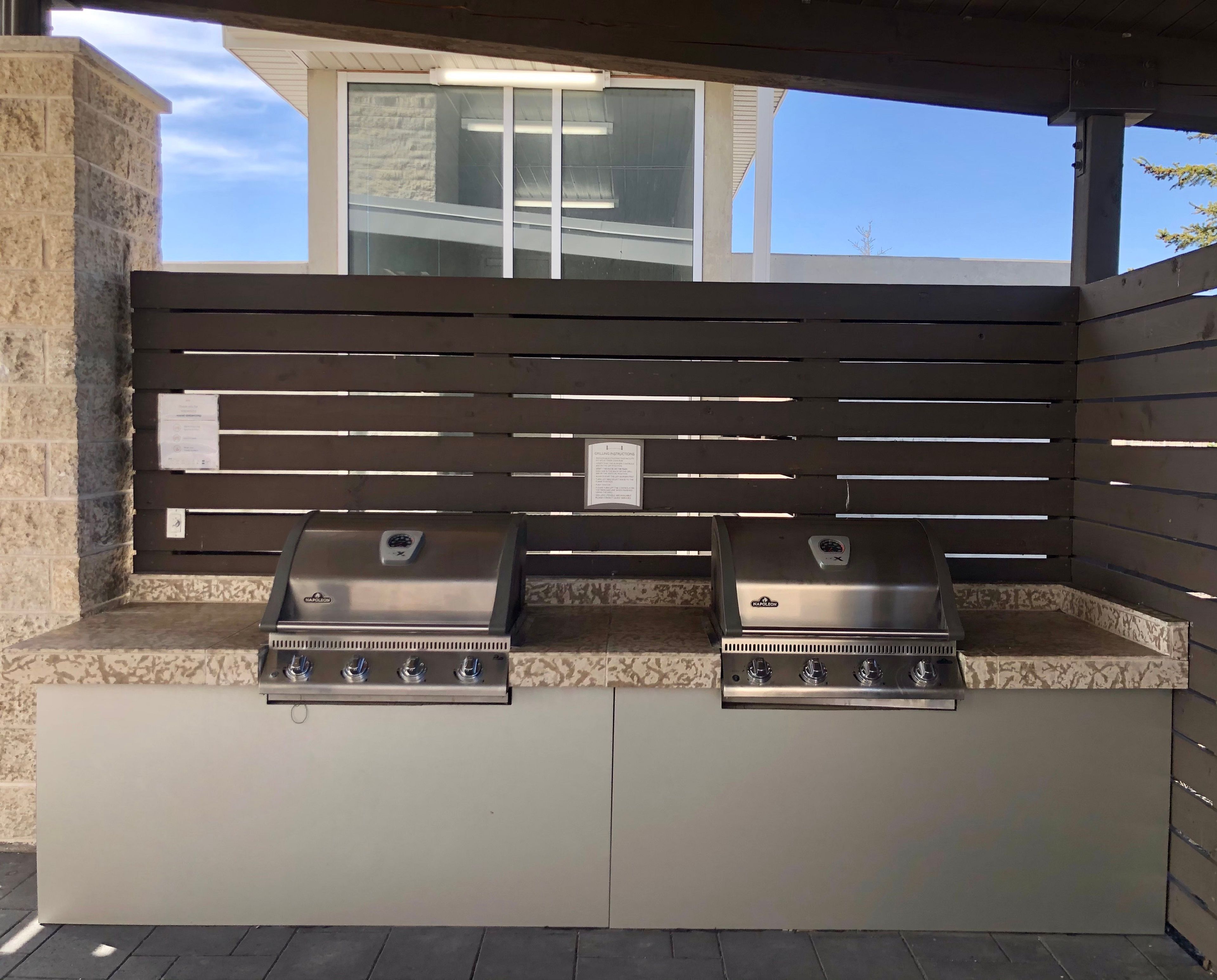 An outdoor grill station with two gas grills, a stone wall, and a wooden fence.