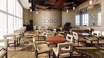 A spacious conference room with multiple tables and chairs, large windows, and a television screen.