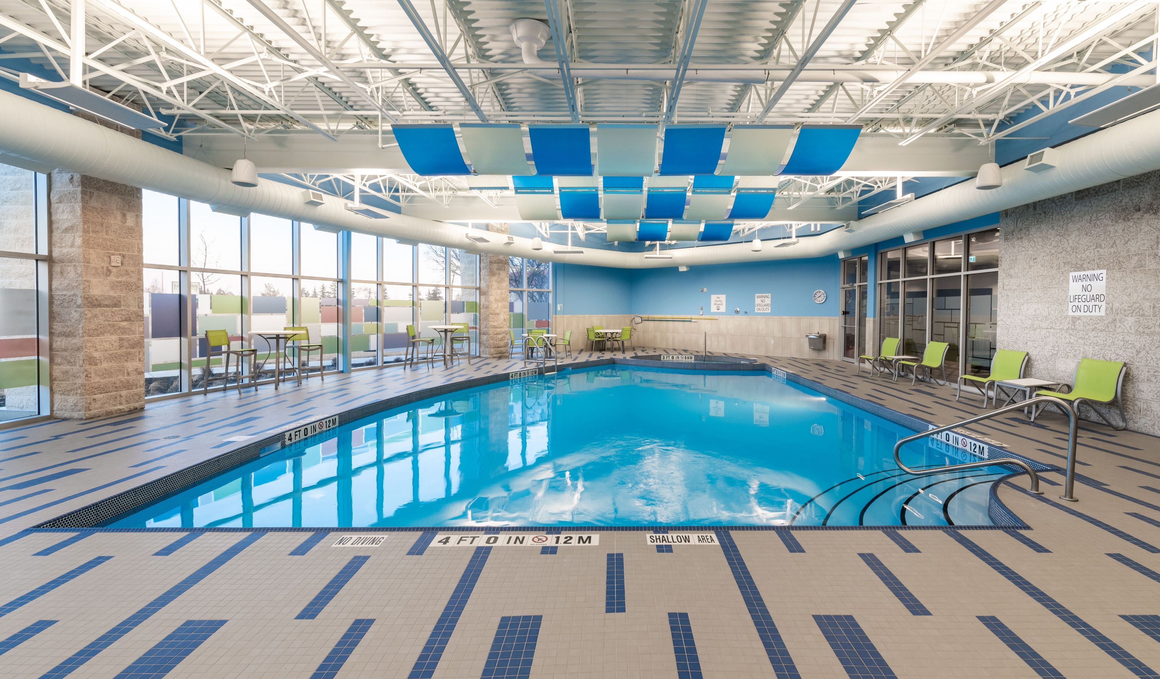 An indoor swimming pool with clear water, marked depth lines, and safety signs.