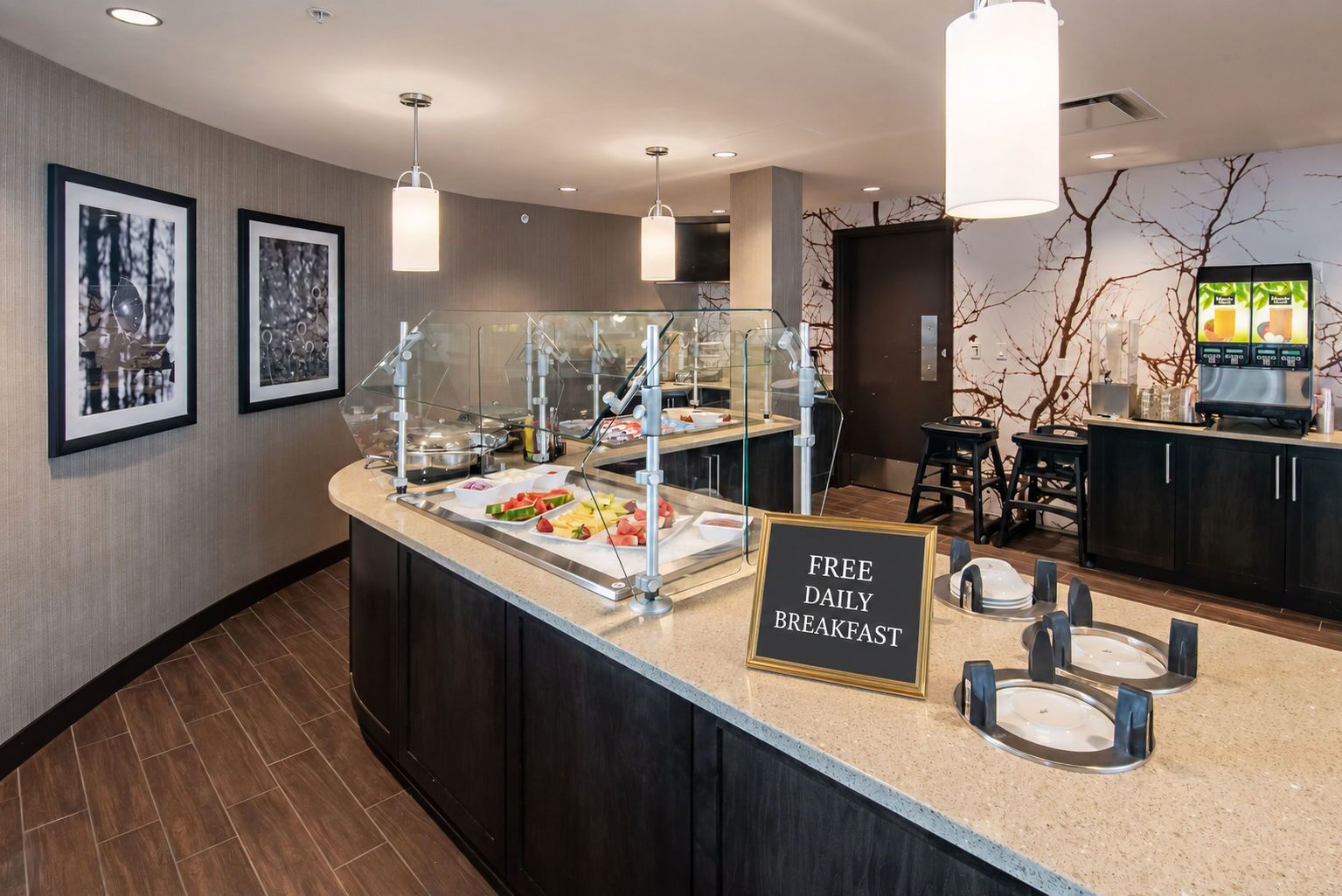 A breakfast bar with a sign offering free daily breakfast, a coffee machine, and framed pictures on the wall.