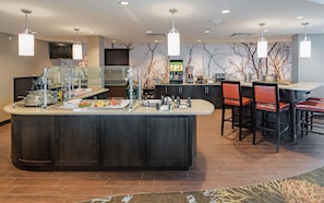 A modern kitchen area with a central island, bar stools, and a seating area.