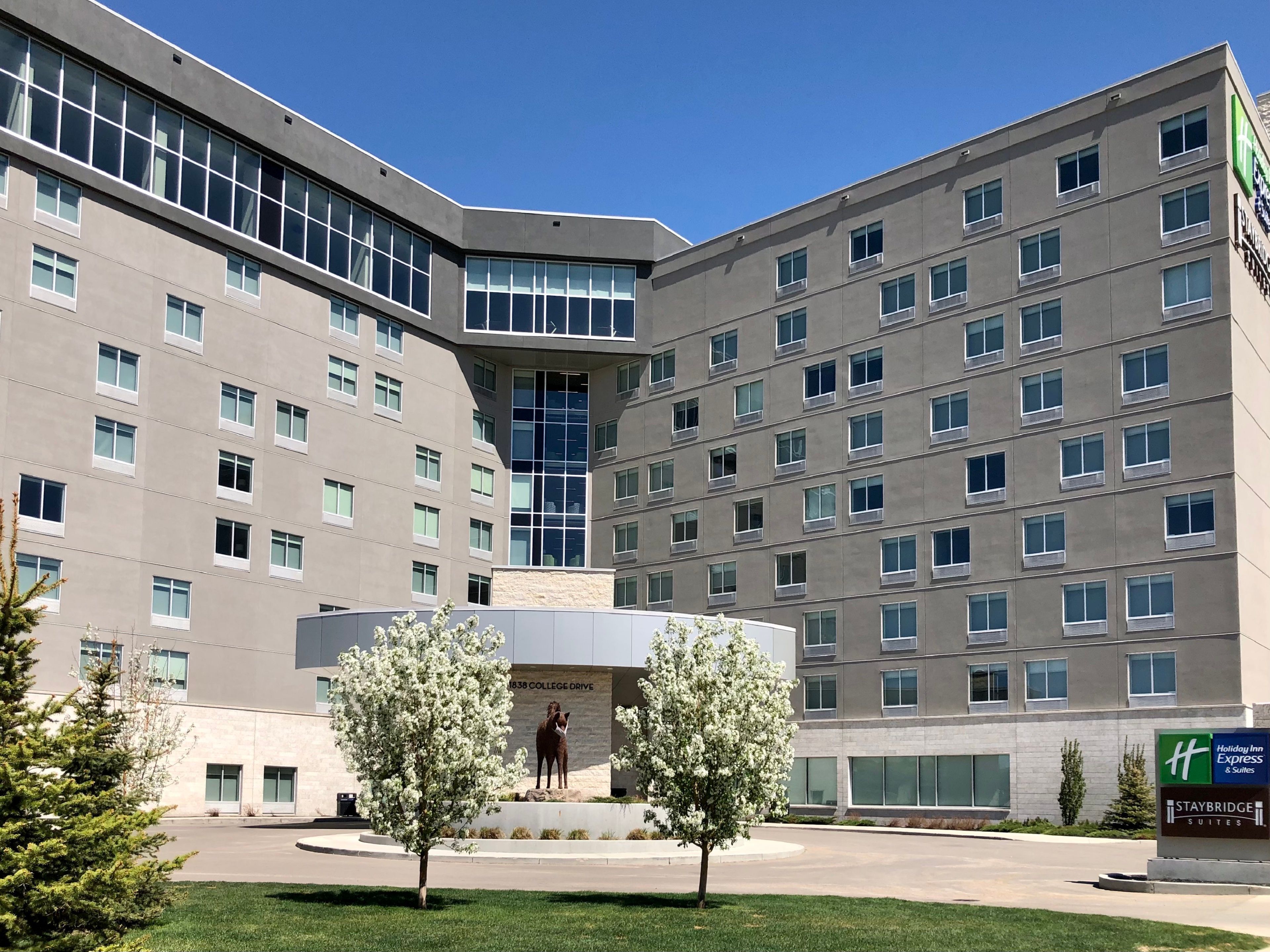 A multi-story hotel with a central courtyard, a statue, and a sign for Holiday Inn Express & Suites Staybridge Suites.