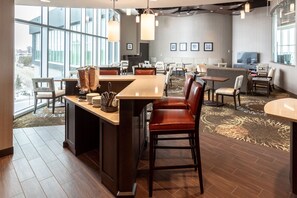 A modern hotel lobby with a central bar area, seating arrangements, and large windows offering city views. - Accessible Suite in Saskatoon | Free Breakfast! (Saskatoon)