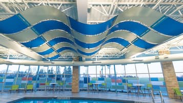 An indoor swimming pool with a wave-like ceiling design, clear glass walls, and multiple seating areas.