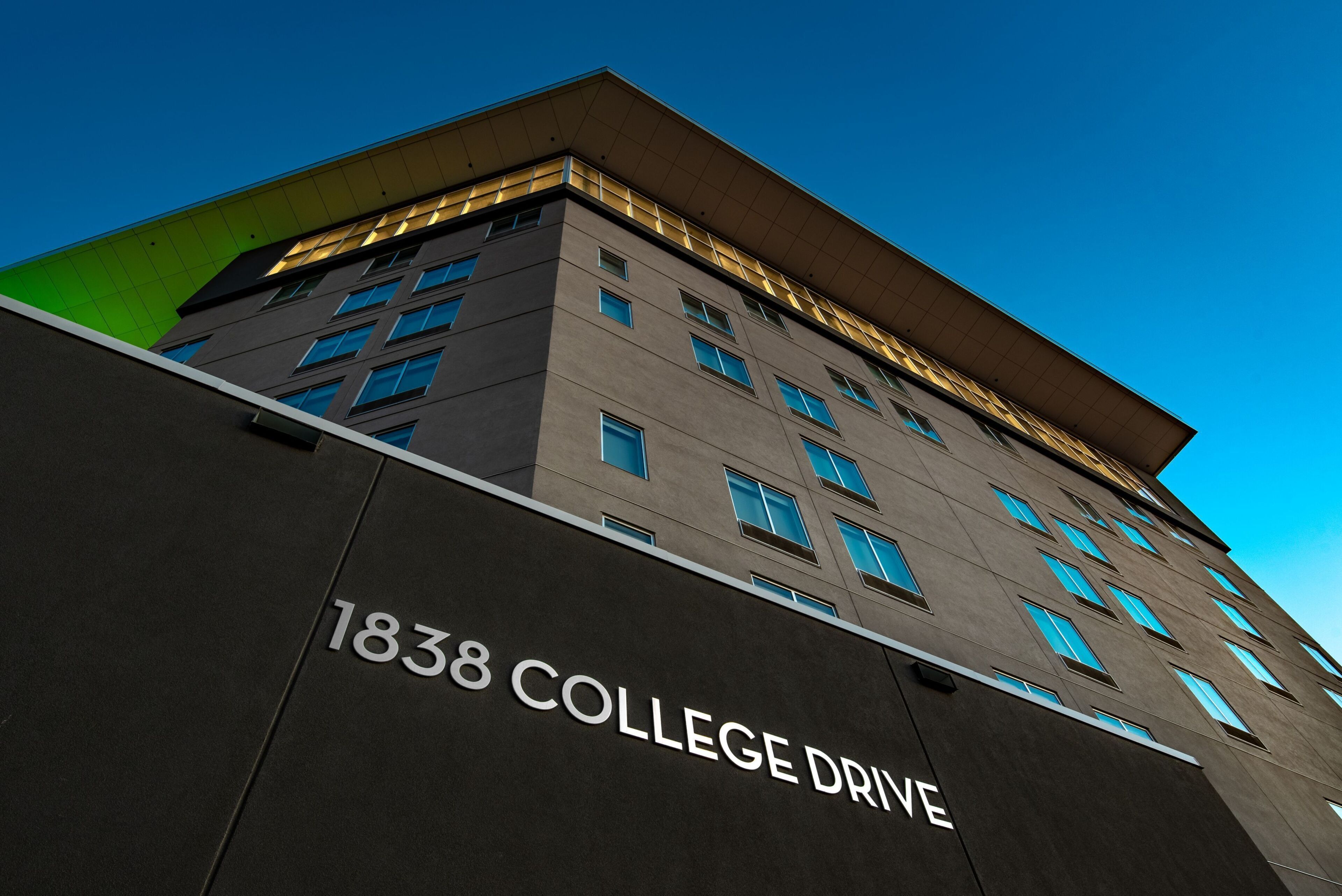 A building with '1838 COLLEGE DRIVE' signage, multiple windows, and a flat roof.