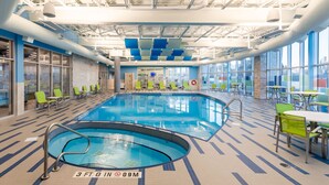 An indoor swimming pool with lounge chairs and tables, large windows, and a tiled floor. - Studio Suite w/ Roll-In Shower | Free Breakfast (Saskatoon)