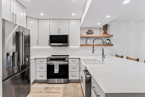 A modern kitchen with stainless steel appliances, white cabinetry, and a central island. - Playa Kas Waterfront Townhouse (Indian Rocks Beach)