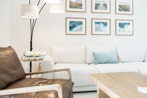 A living room with a sofa, a brown leather chair, a wooden table, and a floor lamp. There are six framed pictures on the wall. - Playa Kas Waterfront Townhouse (Indian Rocks Beach)