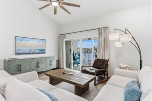 A modern living room with a view of the sea, a balcony with a view of the city, and a large window with curtains. - Playa Kas Waterfront Townhouse (Indian Rocks Beach)