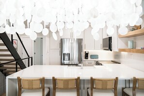 A modern kitchen with a central island, bar stools, and a staircase with a railing. - Playa Kas Waterfront Townhouse (Indian Rocks Beach)