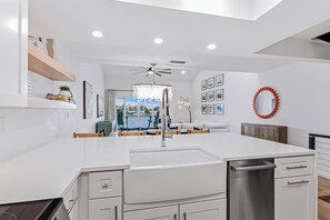A modern kitchen with white cabinetry, a central island, and a view of the outdoors through large windows. - Playa Kas Waterfront Townhouse (Indian Rocks Beach)