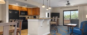 A kitchen with wooden cabinets, a black refrigerator, and a microwave. There is a dining area with a table and chairs, and a balcony with a view. - Cozy 2-bedroom condo in lovely Lake Buena Vista-Close to Disney! (Lake Buena Vista)