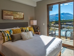 A bedroom with a large bed, a nightstand, a lamp, and a view of a mountainous landscape through a sliding glass door. - Ski-in/out suite at Grand Colorado Peak 8, pools, spa, sleeps 4 • Feb 6-13 (Breckenridge)