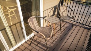A balcony with two wicker chairs and a small table, a glass door, and a metal railing. - Bend river park retreat (Bend)