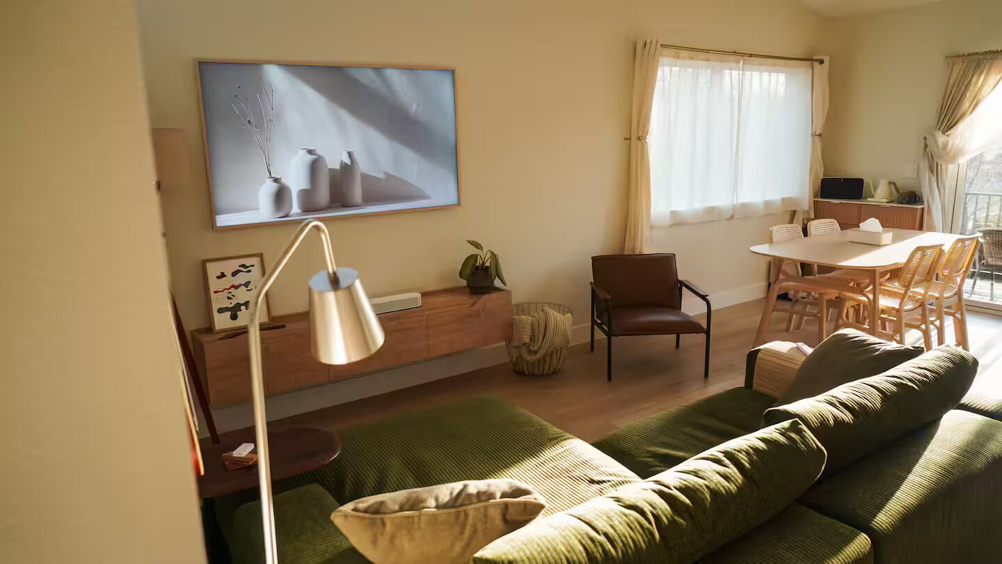 A living room with a sofa, a dining table with chairs, a lamp, and a painting on the wall.