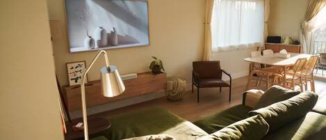 A living room with a sofa, a dining table with chairs, a lamp, and a painting on the wall.