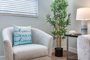 Quarto com poltrona cinza, planta em vaso, abajur e janela na parede.