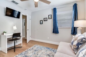 Quarto com escrivaninha, cadeira, televisão e janela com cortinas.