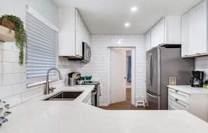 A modern kitchen with white cabinetry, stainless steel appliances, and a central island. - Cozy 2-bedroom house in charming Tampa with AC (Tampa)